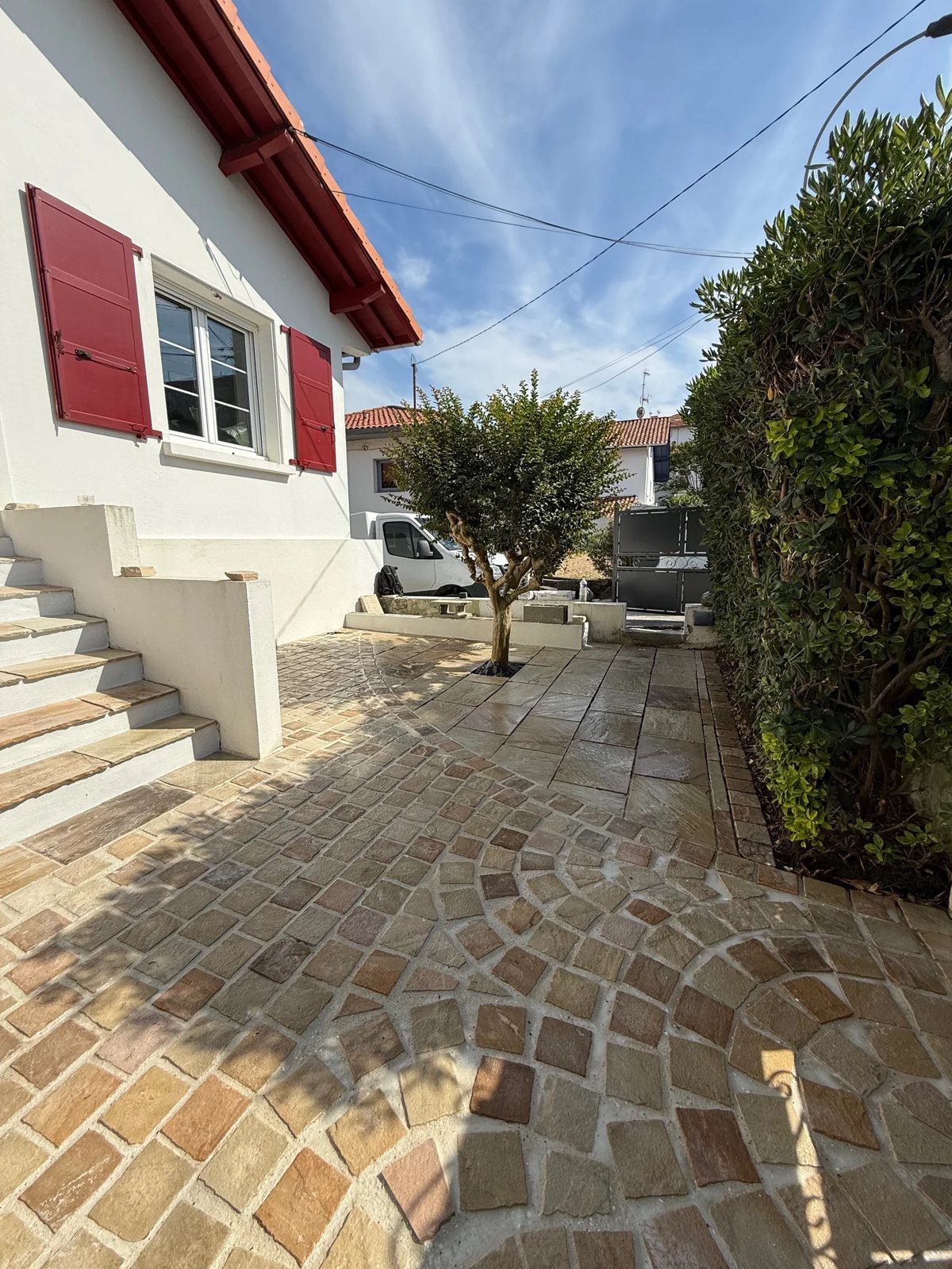 Cour pavée en rosace et dallage de pierre naturelle devant une maison basque aux volets rouges, réalisée par Entreprise Berry