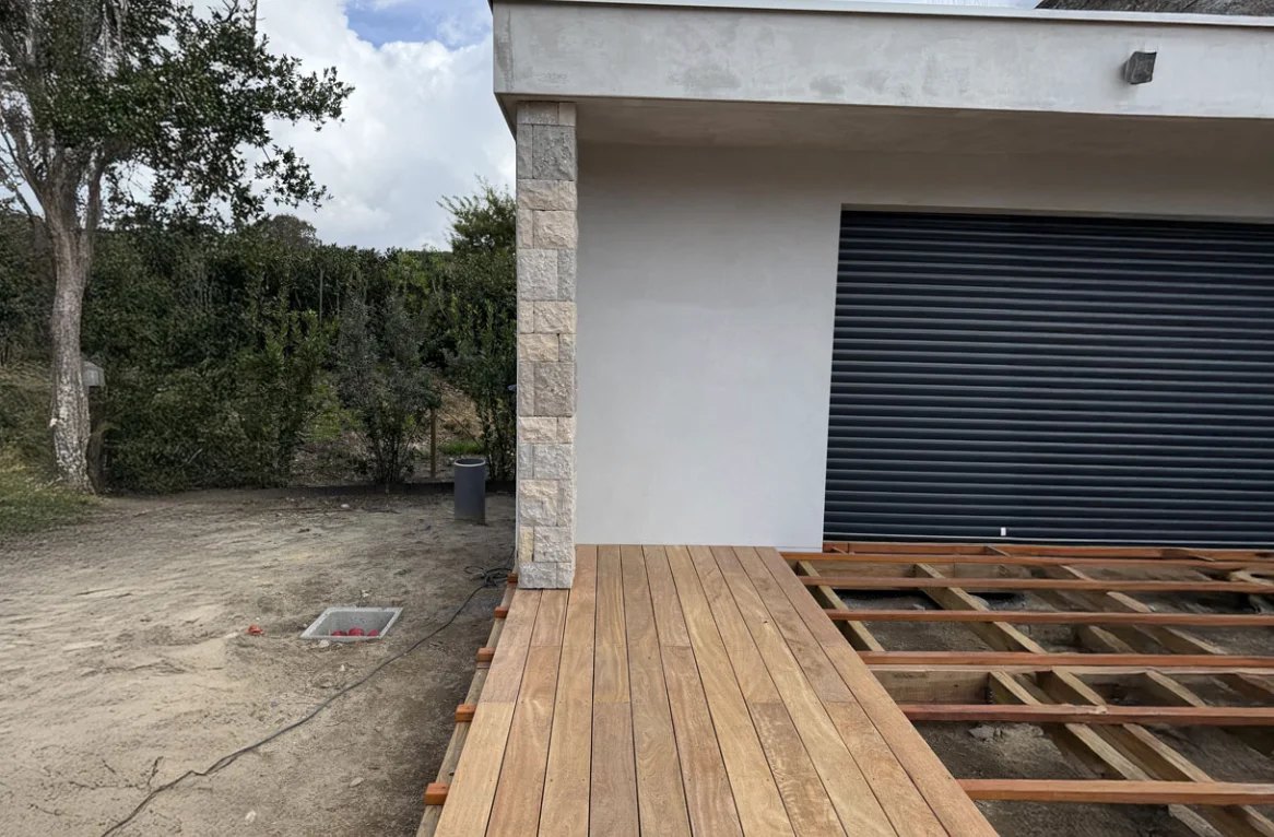 Pilier habillé de pierre à l'angle d'une maison contemporaine, terrasse en bois en cours de pose