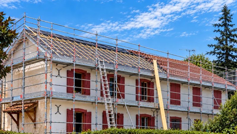 Rénovation complète de toiture sous échafaudage : charpente remise à nu sur une maison aux volets rouges