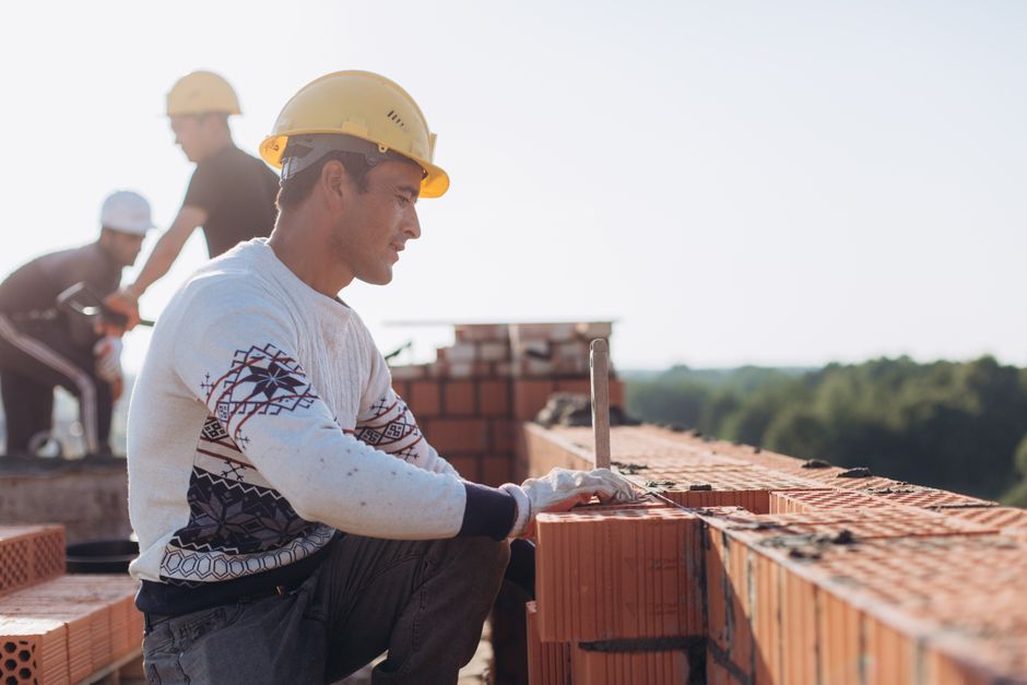 Maçon montant un mur en briques sur un chantier, entouré de son équipe