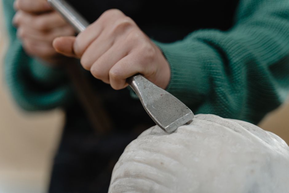 Main d'artisan guidant un ciseau sur une pièce de pierre en cours de taille